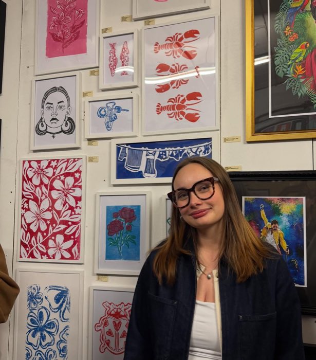 Alice at the opening night of her first art show, a wall of lino prints behind her